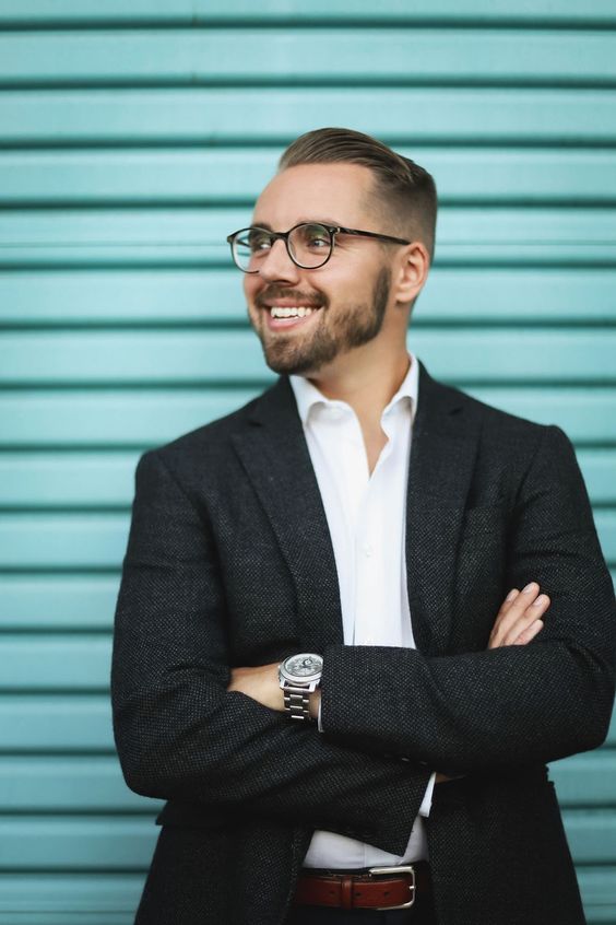 Ben Ortega, Celebrity Exchange Editorial Intern, smiling and wearing glasses and a suit.